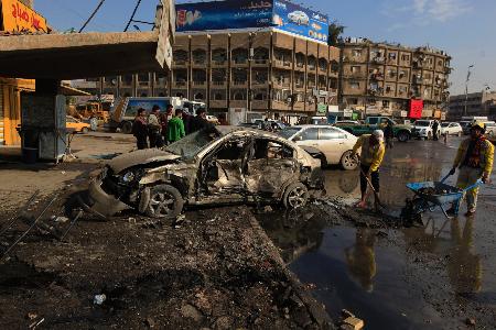 １５日、バグダッドで、爆発した車の様子を見る警察官ら（ロイター）